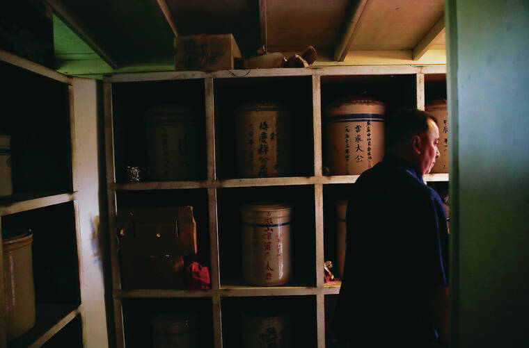 JAMM AQUINO / JAQUINO@STARADVERTISER.COM
                                Robert Wong, grounds superintendent at the Manoa Chinese Cemetery, checks on the ceramic urns holding the remains of immigrants in the Bone House.